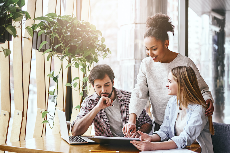 Happy multiracial millennial colleagues discussing company financial statistics at briefing in office, employees brainstorming analyzing growing sales, developing success strategies, reading reports SaaS Sales team discussing new accounting solutions.