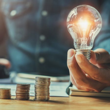 business man hand holding lightbulb with using calculator to calculate and money stack. idea saving energy and accounting finance in office concept